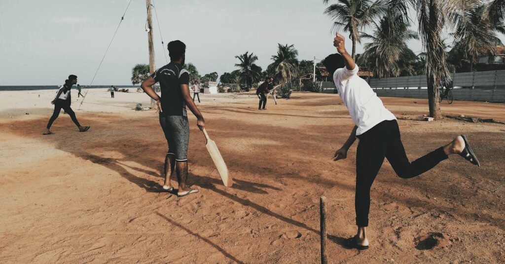 A group of young men playing cricket on a sandy beach under clear skies.